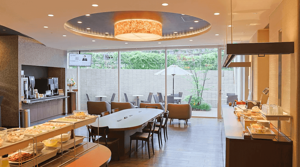 Dormy Inn澀谷神宮前溫泉公共餐廳 Hatago，擁有大面落地窗引入戶外庭園綠意，提供豐盛的自助式早餐，夜晚則變身為提供免費「夜鳴拉麵」的溫馨食堂。