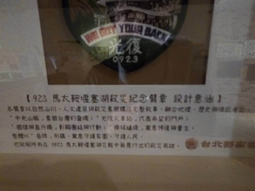 「小旅行迷你公寓」內的【0923 馬太鞍堰塞湖救災紀念臂章 設計意涵】說明牌。 說明牌上方鑲嵌著一枚印有「WE GOT YOUR BACK 光復 0923」字樣的圓形臂章。 下方的文字詳細解說了臂章的設計元素，包含象徵台灣脊樑的中央山脈、代表希望門戶的光復火車站、彰顯團結行動的螺旋槳直升機，以及寓意修復與重生的棒球縫線。 整體設計以「盾牌」形構，象徵守護家園與人民，並向 0923 馬太鞍堰塞湖災難中挺身而出的救災英雄致敬。