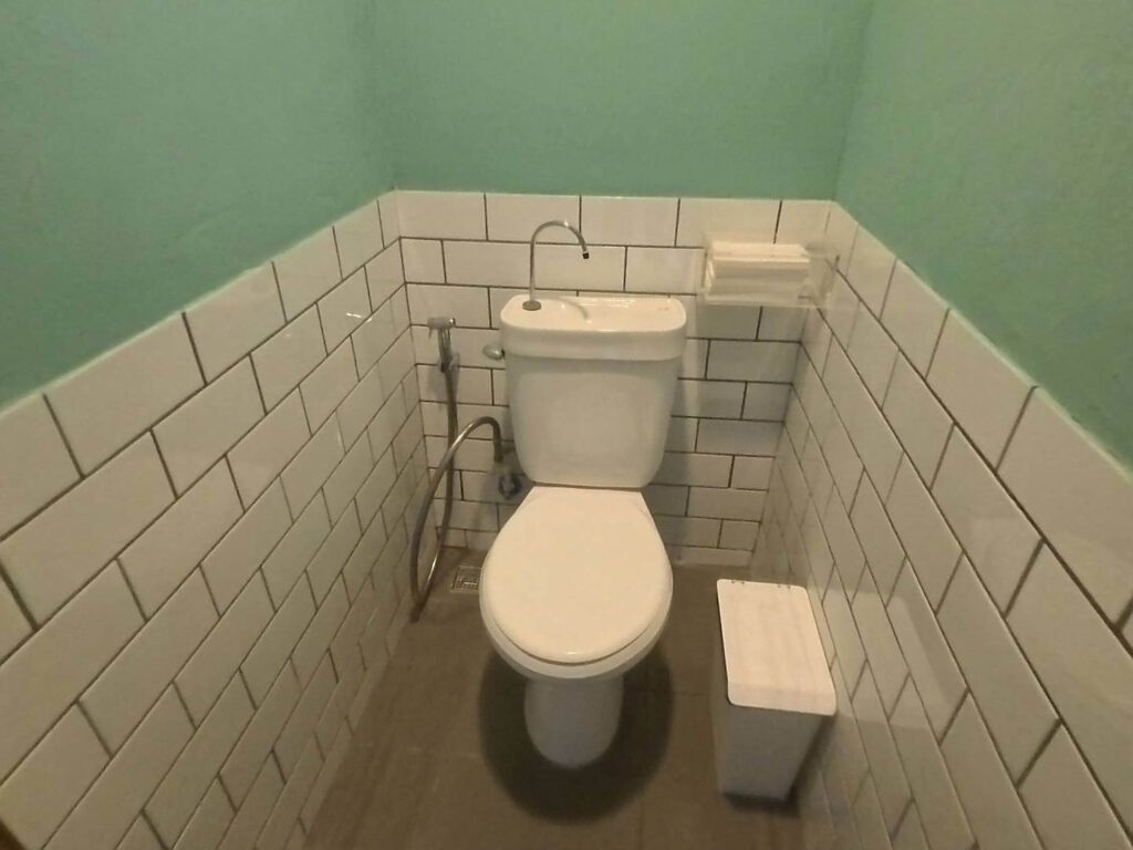 「小旅行迷你公寓（Trip Mini Apartment）的廁所空間，牆面下半部鋪設白色地鐵磚，上半部為湖水綠牆面，配備一體式洗手台馬桶、洗屁屁噴頭及白色簡約垃圾桶。」
