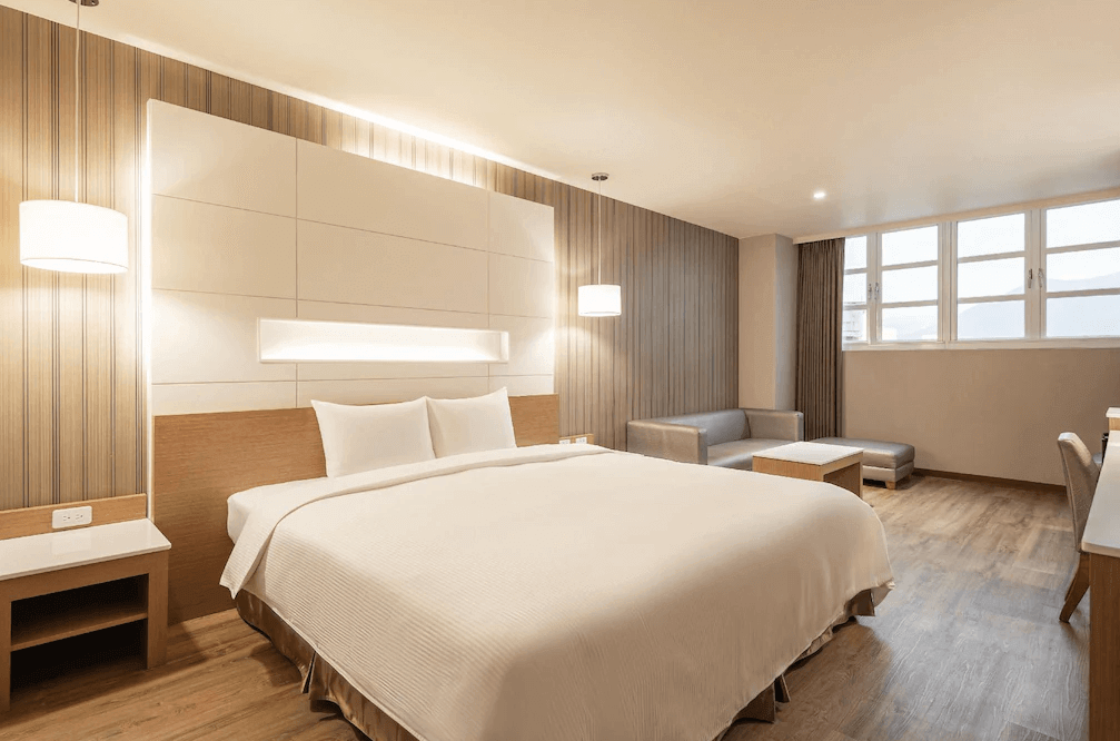 康橋商旅-花蓮站前館的精緻雙人房。室內鋪設溫暖的木地板,配置一張加大雙人床、簡約的小沙發與茶几,窗邊採光充足,呈現溫馨舒適的住宿氛圍。