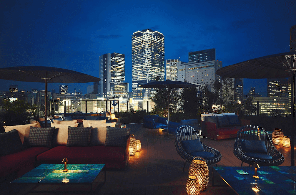 "澀谷住宿精選示意圖"東京澀谷英迪格酒店戶外露台酒吧 (Shibrewya)，擁有開闊的露天座位區與時尚藤編沙發，在夜晚點亮溫暖燈光，是旅客一邊品味調酒、一邊近距離欣賞東京澀谷璀璨夜景的絕佳地點。