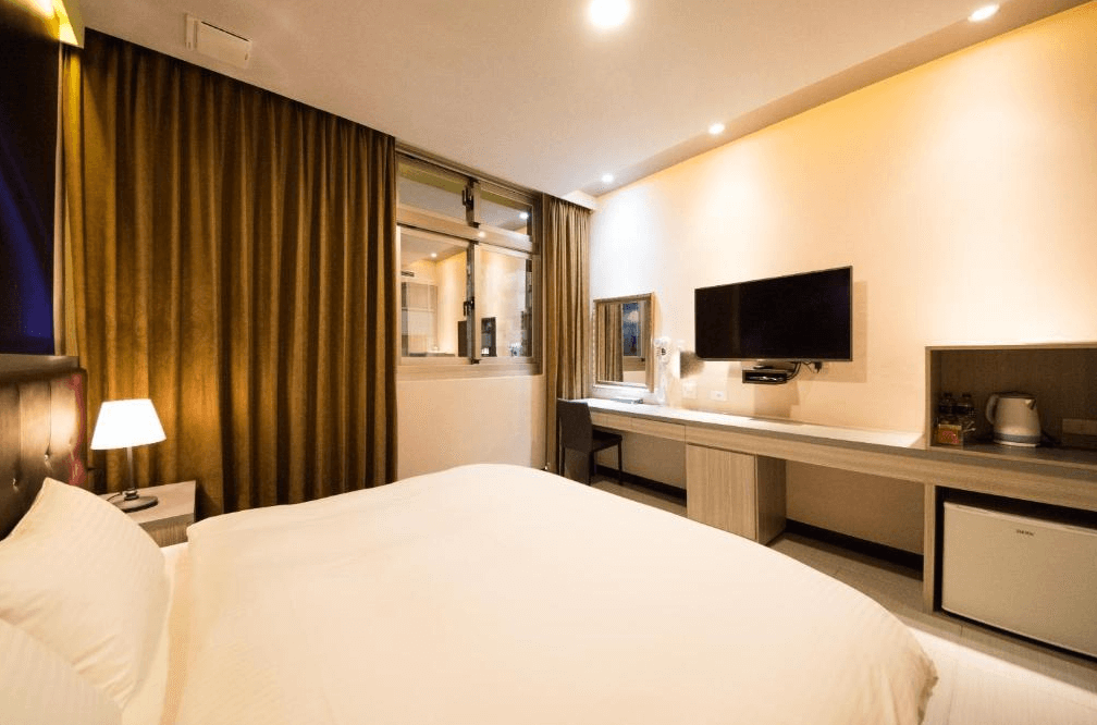 東大門精緻旅店的雙人房型,設有一張大型雙人床與長型簡約書桌,壁掛式電視正對床鋪,旁邊備有電熱水壺與迷你冰箱,提供溫馨的住宿環境。