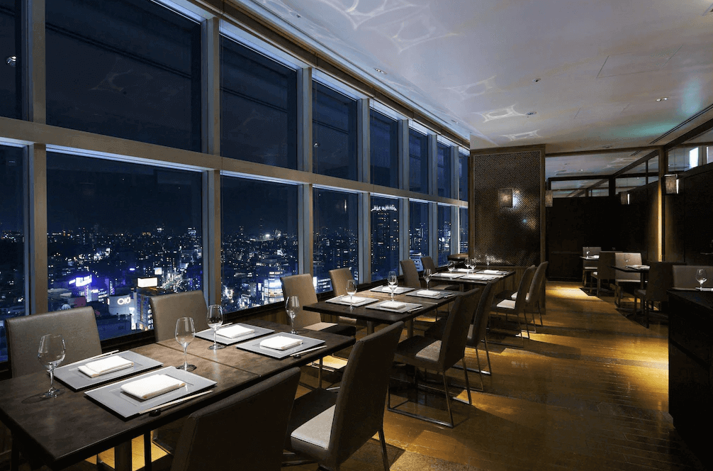 東急澀谷卓越大飯店高空景觀餐廳，夜晚時分窗外呈現璀璨迷人的澀谷都市夜景，室內燈光微醺浪漫，座位區沿著窗邊設置，是享受精緻晚餐與欣賞東京夜色的絕佳場域。