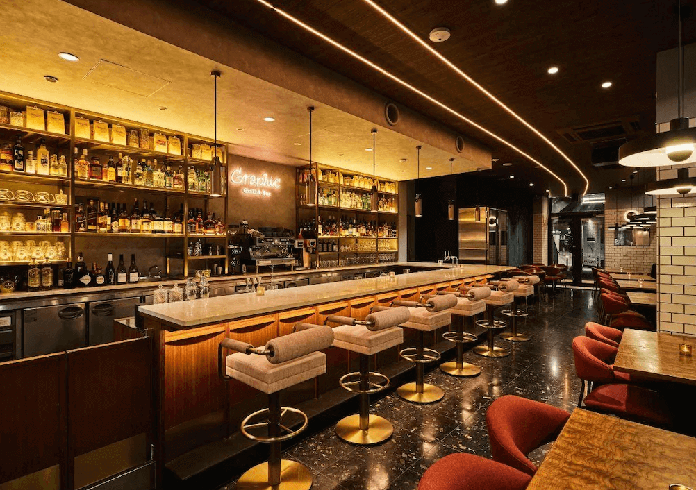 澀谷格拉菲飯店附設酒吧餐廳，吧台區設計充滿復古工業風，暖黃色燈光投射在擺滿酒瓶的層架與質感高腳椅上，提供住客小酌放鬆、享受微醺夜生活的社交空間。