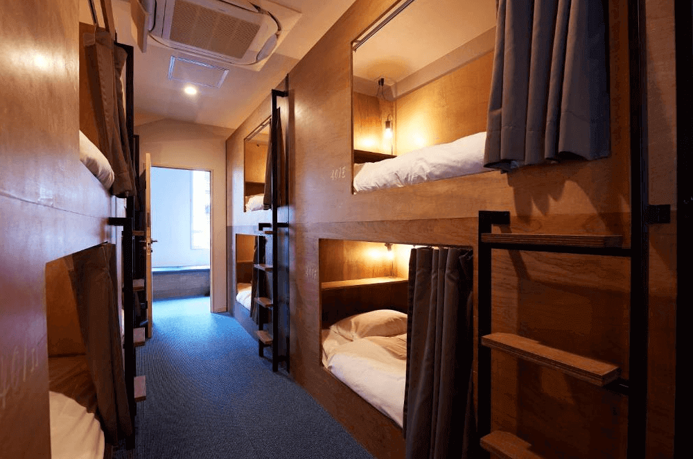 留聲機青年旅舍宿舍房（Dormitory），採用溫潤的木質膠囊式上下舖設計，每個床位皆配有厚實的遮光簾與專屬閱讀燈，為背包客提供極具安全感與隱私的睡眠空間。