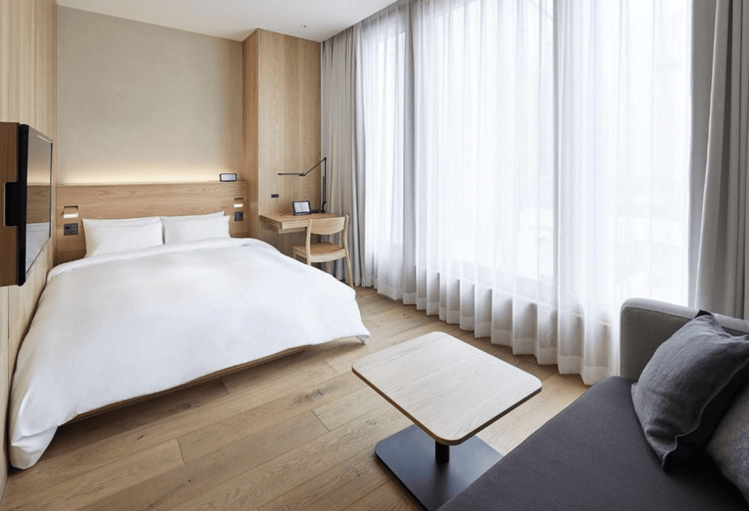 MUJI HOTEL GINZA飯店大廳，以大量粗糙舊木樑裝飾天花板，櫃檯採用單塊粗糙質感長木桌，並保留原始圓柱石柱與日式「和」字暖簾，營造極簡自然的接待空間。