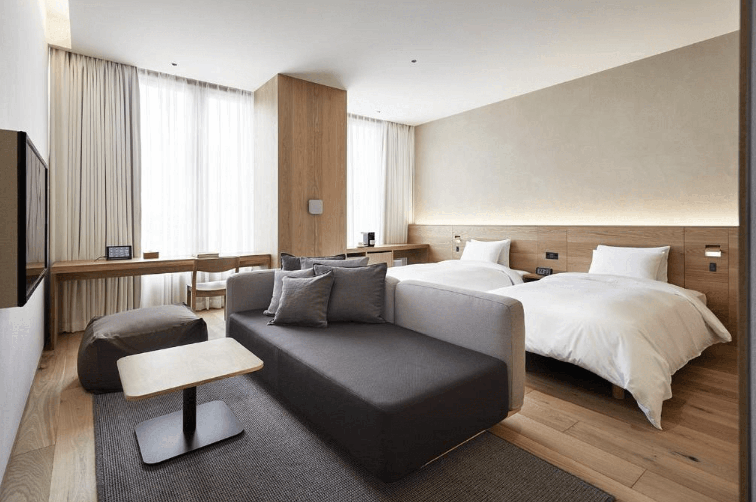 MUJI HOTEL GINZA客房內的溫馨休息角落，配置無印良品單人椅與小茶几，牆面嵌有書架陳列書籍與藝術品，窗外可見銀座繁華街景，氛圍寧靜放鬆。