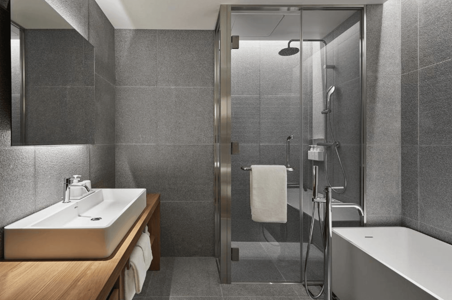 MUJI HOTEL GINZA寬敞的客房L型休息與用餐區，設有大型灰色布面沙發、低矮長木桌與圓形餐桌，空間充滿無印良品簡約日式設計感。