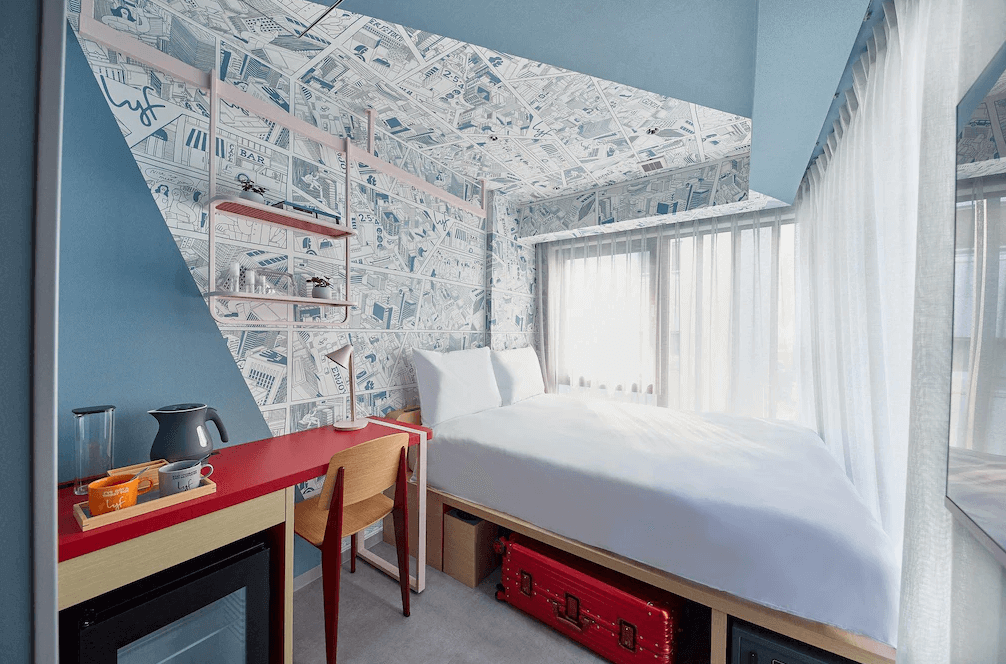 lyf銀座東京特色客房，牆面與天花板採用極具設計感的城市手繪地圖壁紙，搭配搶眼的紅色長型書桌，床架下方更巧妙規劃了專屬的行李箱收納空間，展現年輕活潑的創意巧思。