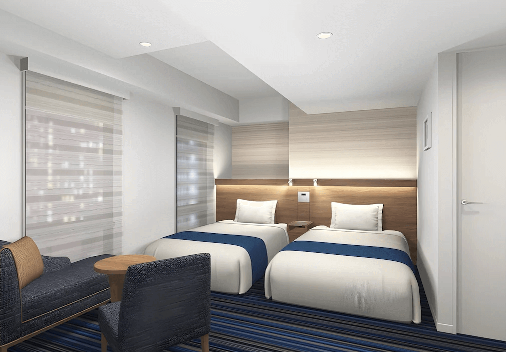 京王布萊索飯店東京站八重洲精緻雙床客房，床頭設計簡練並設有專屬閱讀燈，靠窗處特別配置了深藍色沙發休憩區與小圓桌，提供旅客在都會中放鬆的實用角落。