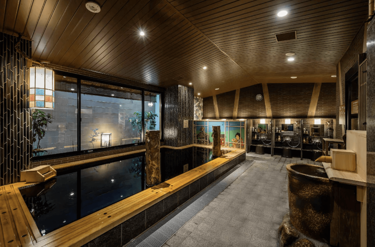 凌雲之湯 御宿野乃的天然溫泉大浴場實景，寬敞的黑色溫泉池周邊以木頭收邊，牆面裝飾有傳統日式畫作，整體空間充滿療癒感