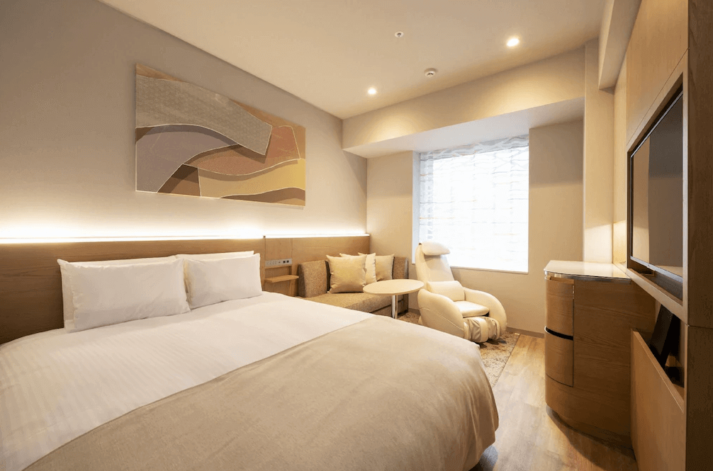 東京京橋雷姆飯店舒適雙人房，以溫潤的淺色木質調與純白床鋪為主，房內最大亮點是靠窗處配備了專屬的白色頂級按摩椅，讓旅客能在溫馨放鬆的空間中卸下整日的旅途疲憊。