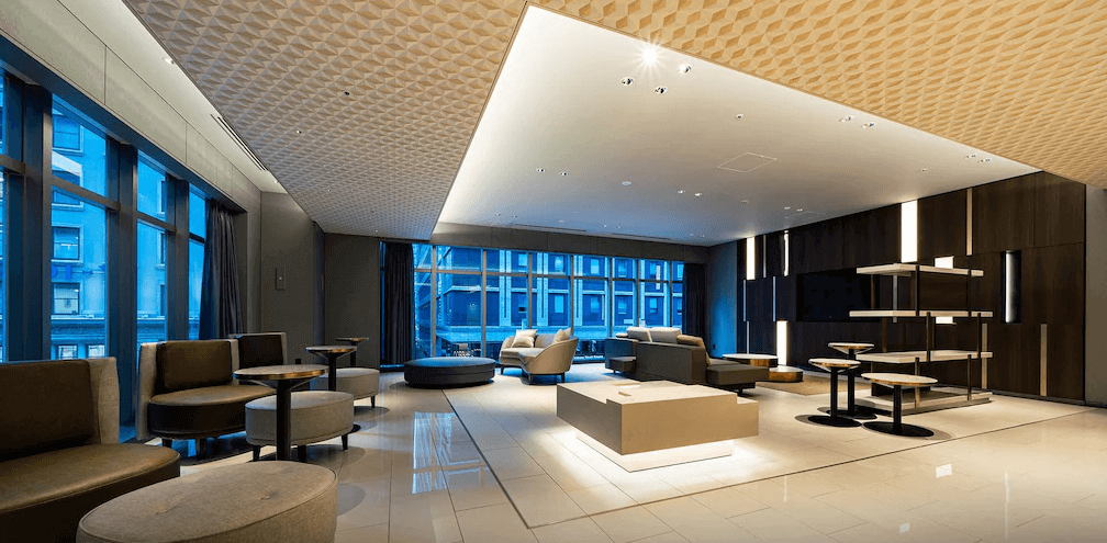 東京京橋大及魯內普米爾飯店公共交誼大廳，天花板採用獨特且精緻的幾何菱格紋設計，搭配大面景觀落地窗與充滿現代設計感的沙發休憩區，展現低調奢華的都會商務質感。