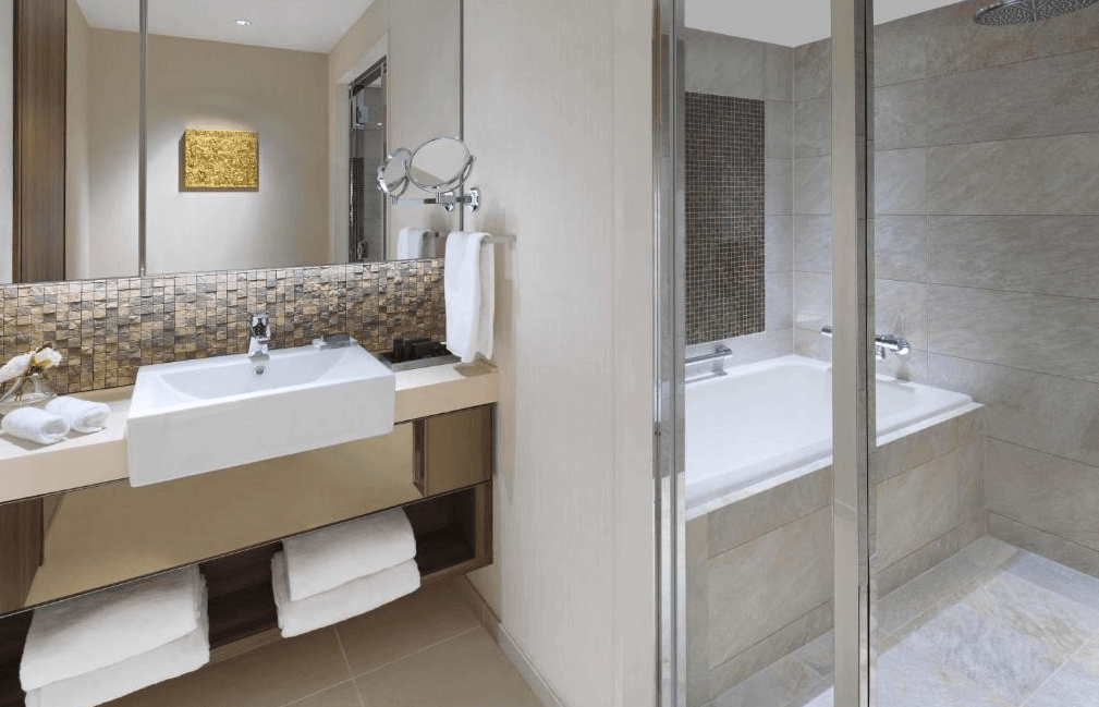 東京奧克伍德尊貴酒店質感衛浴空間，採用明亮溫潤的石紋磁磚打造，配備獨立的透明玻璃淋浴間、深型泡澡浴缸與寬敞的現代感洗手台，提供如頂級SPA般的沐浴享受。
