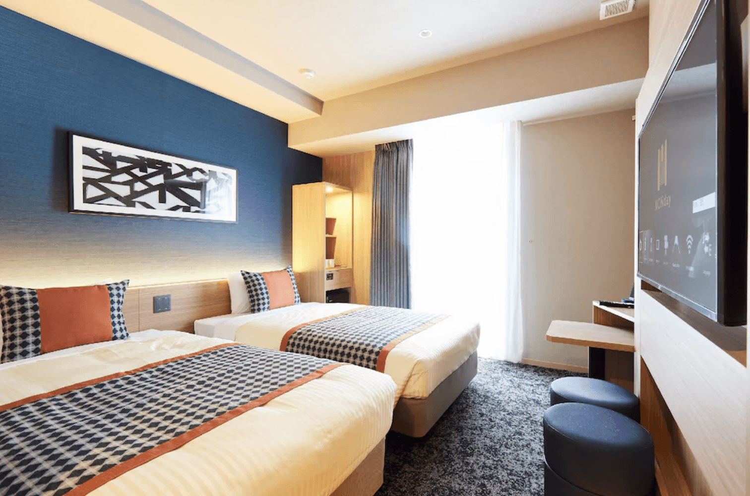 現代化的雙人床房型實景。牆面以沉穩的藍色為底，掛有簡約的抽象畫作。房內配有兩張單人床、壁掛電視及質感地毯，採光良好且氛圍溫馨
