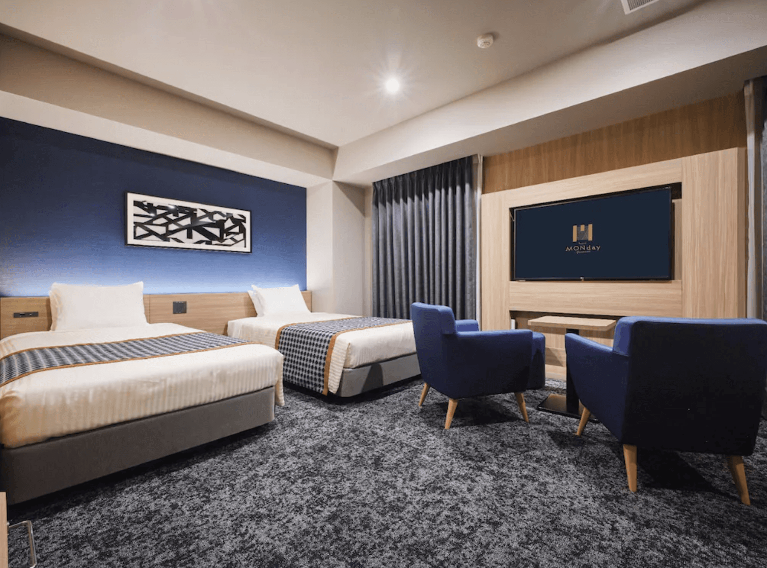 空間較為寬敞的高級房型，設有兩張單人床及兩張藍色單人沙發對坐區。電視牆結合了溫潤的木質面板，整體設計洗練且充滿現代感