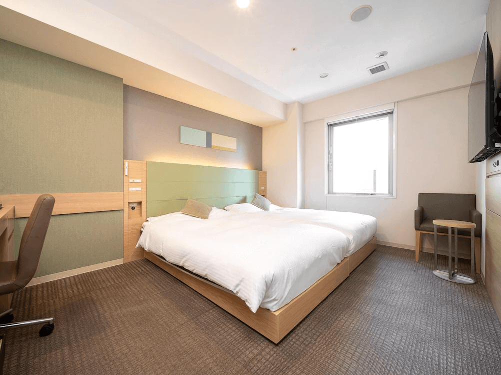 東京站八重洲中央口超級精選飯店舒適雙床房，床頭採用清新的淺綠色調裝飾板，搭配溫潤的淺色木質床架與實用辦公桌，整體空間設計簡約明亮，帶有品牌特有的樂活（LOHAS）放鬆氛圍。