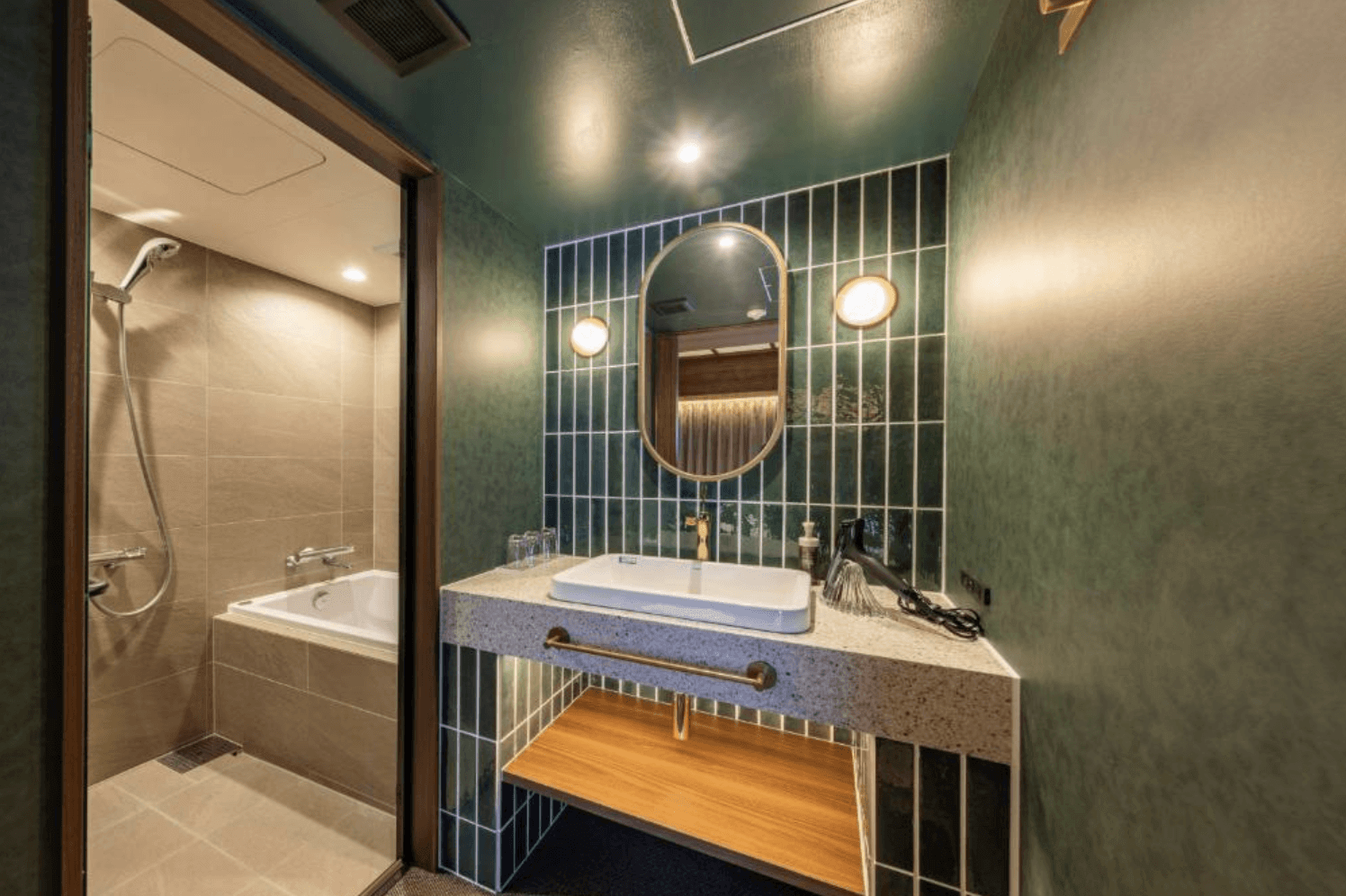 淺草京阪飯店 (Hotel Keihan Asakusa) 客房內現代風格的衛浴設施。深綠色牆面搭配大理石紋理洗手台與金邊圓鏡，並設有乾濕分離的獨立淋浴間與浴缸