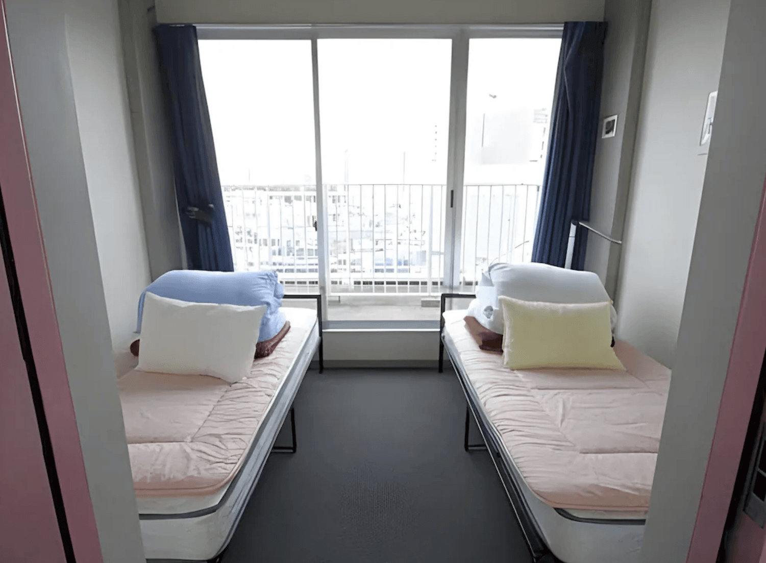 淺草櫻花青年旅館的簡約客房，房內設有兩張對齊的單人床位，盡頭設有大面落地窗與陽台，採光良好且環境整潔