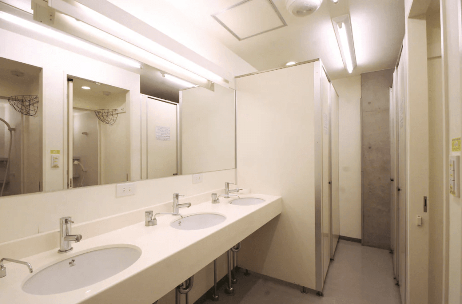 淺草櫻花青年旅館的公共衛浴空間，配備多個整潔的洗手台、大面梳妝鏡以及獨立的淋浴間與廁所設施