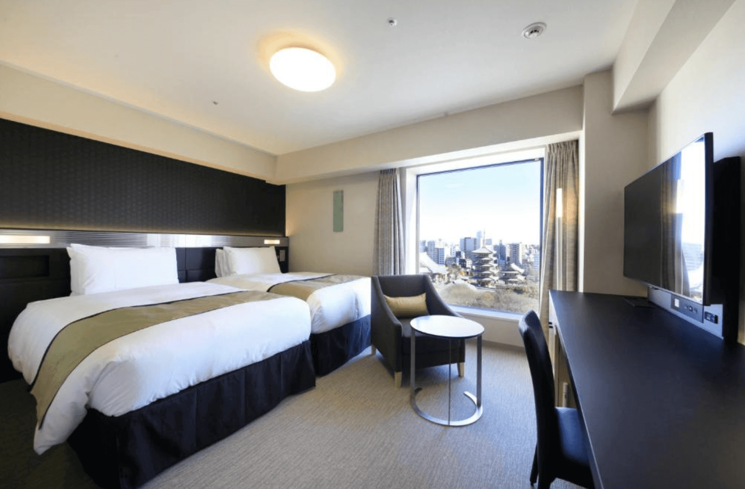 里士滿淺草國際酒店的雙床房日間實景。房間整潔明亮，配有兩張單人床、一張扶手椅和小圓桌、一條長書桌和電視。大片落地窗外可欣賞到淺草寺和五重塔的壯麗日間景色