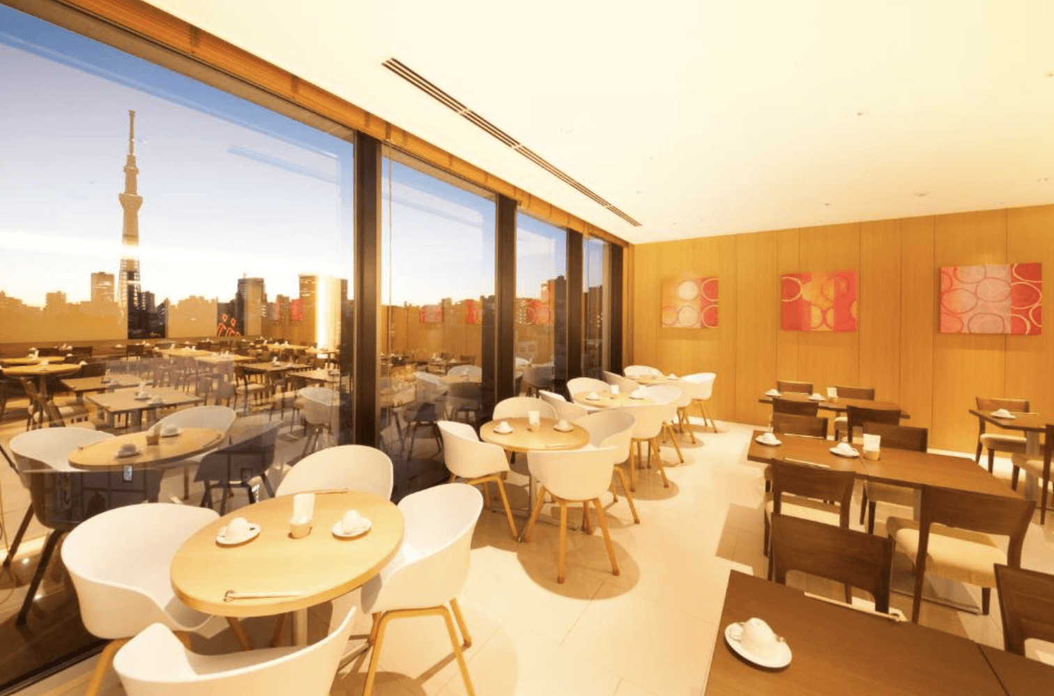 里士滿淺草國際酒店的餐廳。餐廳採用現代典雅的木質裝潢，白色桌椅整齊排列，牆上掛著圓形圖案的裝飾畫。大片落地窗外，東京晴空塔矗立在城市景觀中