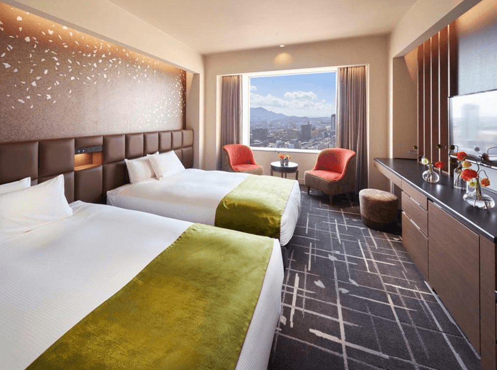 北九洲小倉麗嘉皇家飯店 (Rihga Royal Hotel Kokura Fukuoka)1.jpg
飯店雙人房實景。房間內有兩張單人床，床尾鋪著綠色床旗。牆面裝飾有細緻的櫻花圖案，大片景觀窗可俯瞰北九州市景與遠山，室內配置兩張紅色沙發椅與圓几