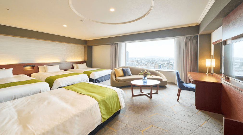 北九洲小倉麗嘉皇家飯店 (Rihga Royal Hotel Kokura Fukuoka)2.png 飯店寬敞的家庭房或四人房。室內擺放四張單人床，床旗皆為綠色。靠窗處設有一座弧形沙發與咖啡桌，採光極佳，窗外為開闊的城市景觀，整體設計簡約典雅。