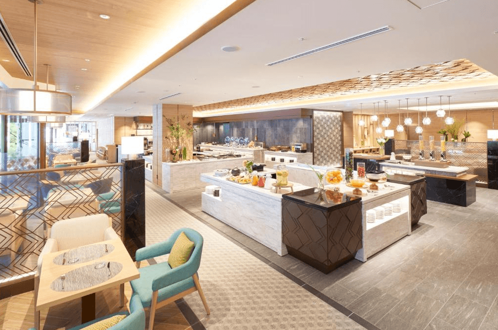 北九洲小倉麗嘉皇家飯店 (Rihga Royal Hotel Kokura Fukuoka)4.jpg 飯店自助餐廳（Buffet）的環境。空間設計明亮且具現代感，採用大量的木質元素與大理石檯面。取餐區排列整齊的各式佳餚與飲品，用餐區配有淺藍色舒適沙發椅。