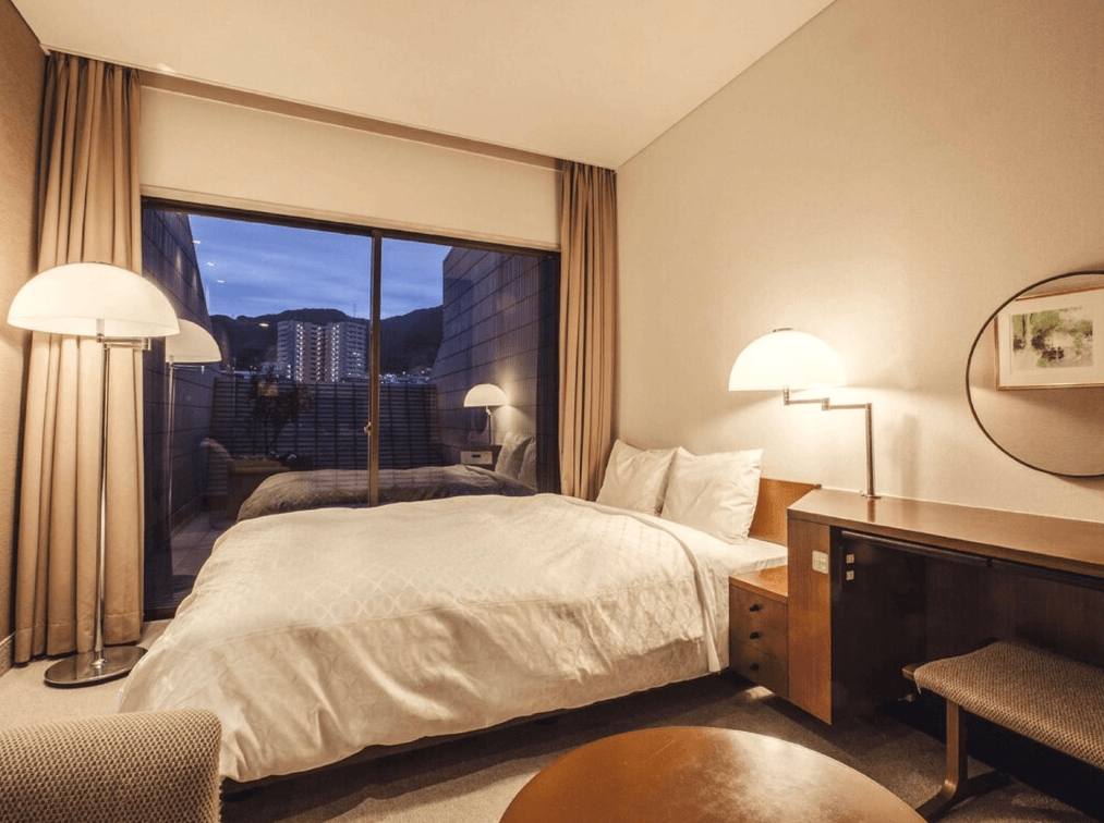 千草酒店 (Chigusa Hotel)1.jpg
飯店單床房實景。房間設計溫馨，配有一張雙人床，床頭設有半圓形時尚壁燈。床側有一張木質長型書桌，上方掛有圓形鏡子。大片落地窗外是一個小陽台，可看見北九州的城市夜景，燈光氛圍優雅舒適。