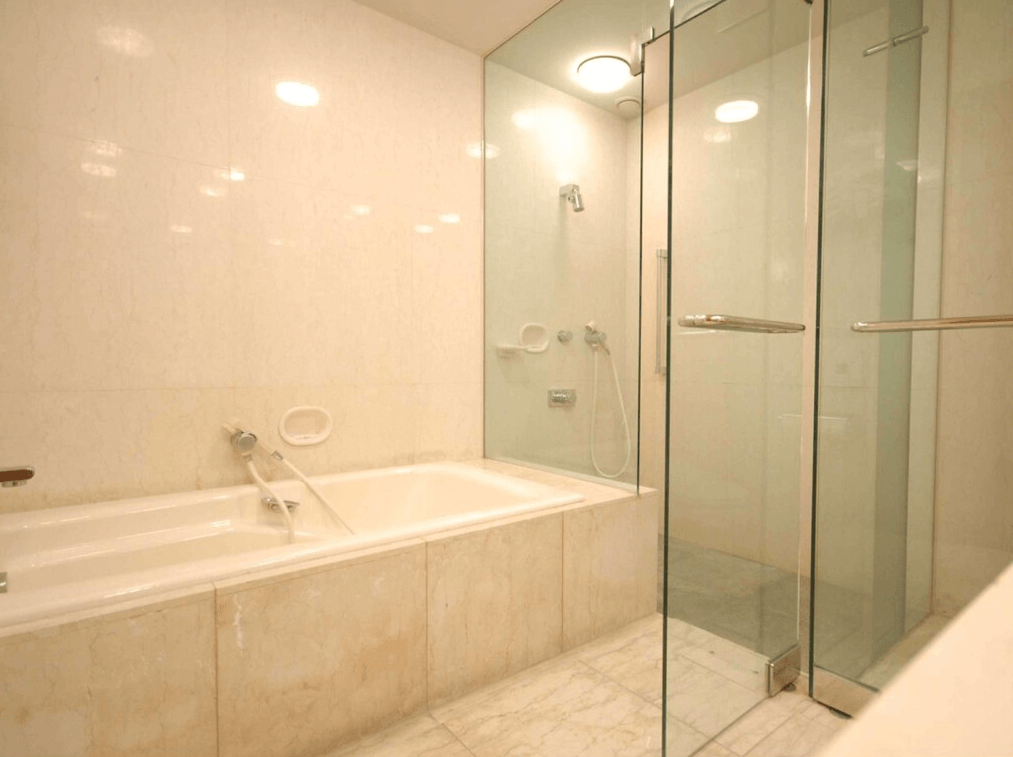 千草酒店 (Chigusa Hotel)3.jpg 飯店客房衛浴空間。牆面與浴缸外側皆鋪設淺米色大理石紋磁磚。淋浴區與浴缸並列，並由透明玻璃隔斷，採乾濕分離設計。空間明亮、簡潔且具備現代感。