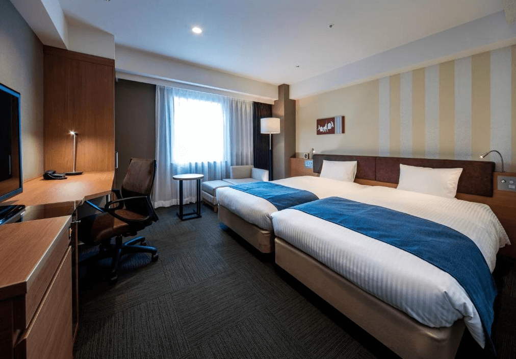 大和Roynet飯店 - 小倉站前 (Daiwa Roynet Hotel Kokura-Ekimae)1.png
飯店標準雙床房實景。房間內配置兩張單人床，床尾鋪有藍色床旗。左側靠牆處有一張長型木質辦公桌與黑色辦公椅，窗邊設有小圓几與單人沙發床，整體風格現代且功能齊全。