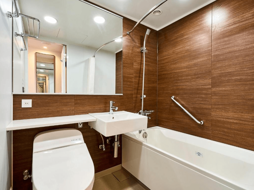 大和Roynet飯店 - 小倉站前 (Daiwa Roynet Hotel Kokura-Ekimae)3.jpg 飯店客房的衛浴空間。浴室牆面採用深色木紋飾板，配備白色浴缸與免治馬桶。洗手台上方裝有大面積鏡子，空間乾淨明亮，展現典型的日式商務飯店精緻風格。