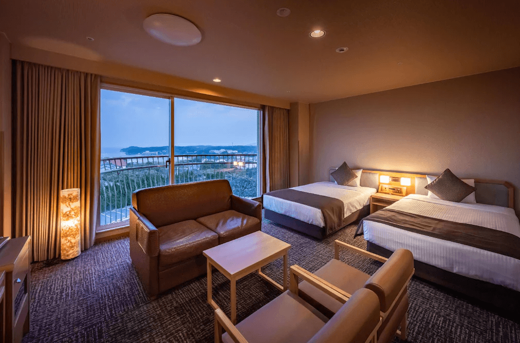 玄界灘龜之井飯店 (KAMENOI HOTEL GENKAINADA)1.jpg
飯店雙床房實景。房間空間寬敞，配置兩張單人床與深棕色皮質沙發組。落地窗旁擺放著一盞透著溫暖橘光的日式圓柱燈。透過窗戶可遠眺傍晚時分的玄界灘海景與沿岸燈火，氛圍沉靜舒適。