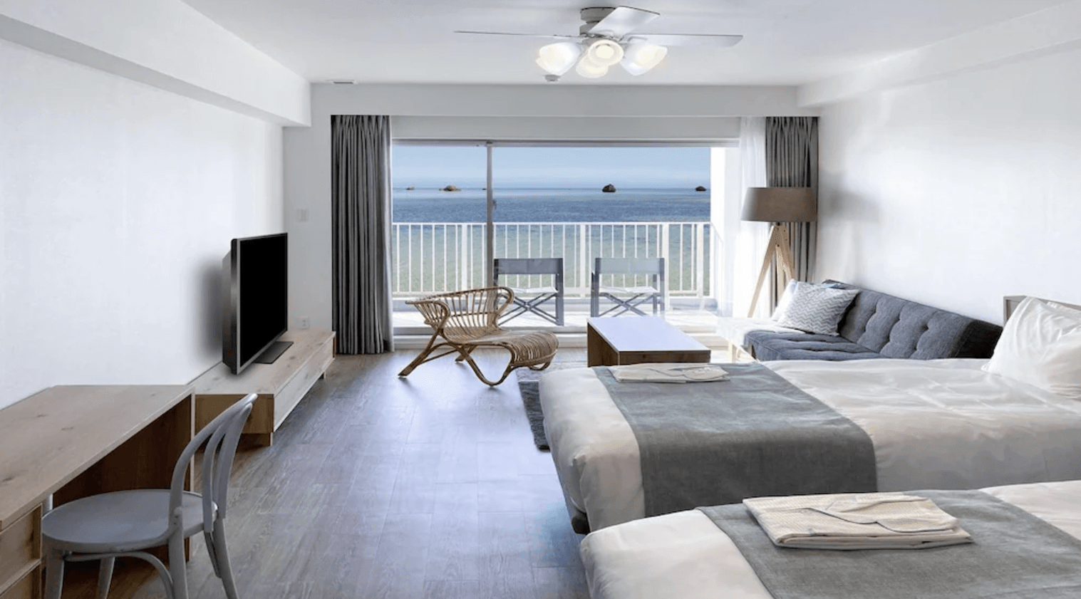 沖繩宮古島水印飯店 (Watermark Hotel Okinawa Miyakojima) 的明亮海景雙床客房。房內鋪設淺色木質地板，配有兩張舒適的單人床、灰色沙發、藤編休閒椅與電視，並設有大片落地窗可通往專屬陽台，讓住客能直接欣賞充滿礁岩點綴的蔚藍海景。
