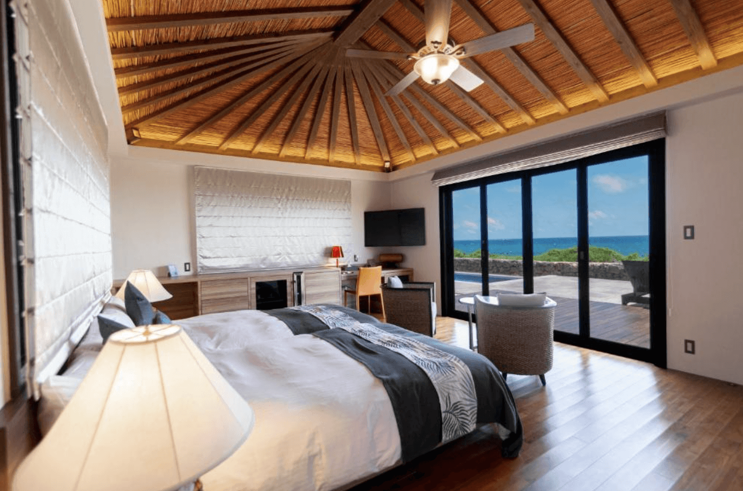 維拉布度假酒店 (Villabu Resort) 的豪華海景客房，房內有著挑高的特色茅草圓錐形屋頂與吊扇，寬敞的雙人床面向大片落地窗，可直接通往戶外露台並欣賞湛藍海景。
