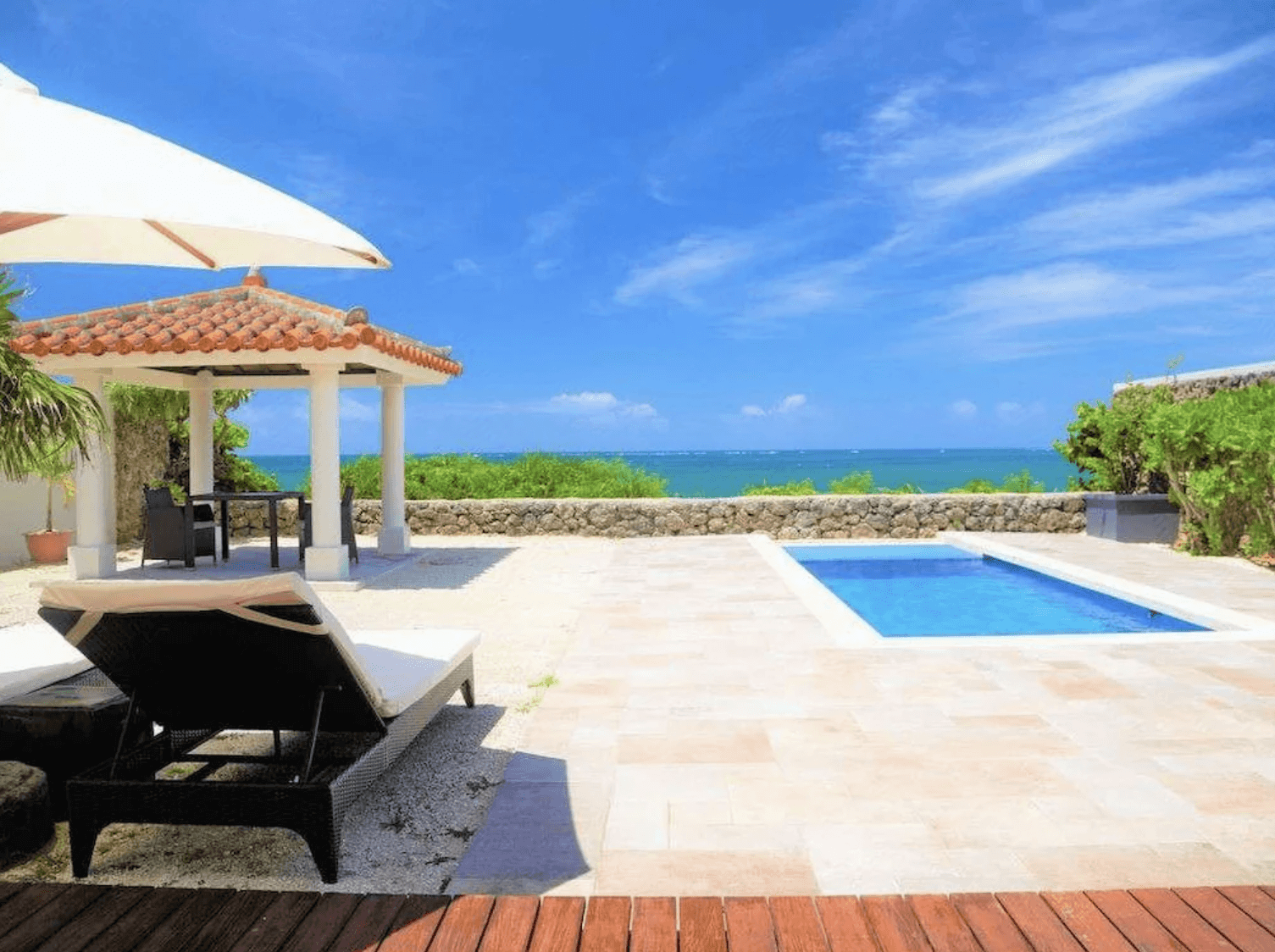 維拉布度假酒店 (Villabu Resort) 的私人戶外露台與泳池，設有舒適的躺椅、遮陽傘與一座戶外涼亭，前方以矮石牆隔開，外頭即是一望無際的蔚藍海洋與晴空。