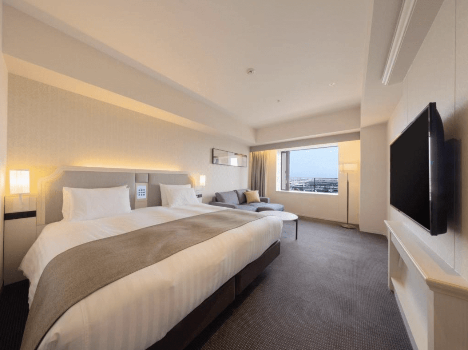 以下是為您按順序產生的圖片替代文字:
大阪LIBER酒店 (LIBER HOTEL OSAKA) 的現代化雙人客房,房內鋪設深色地毯,設有寬敞舒適的雙人床,並配有靠窗的灰色沙發、茶几與壁掛式電視,設計簡約雅緻