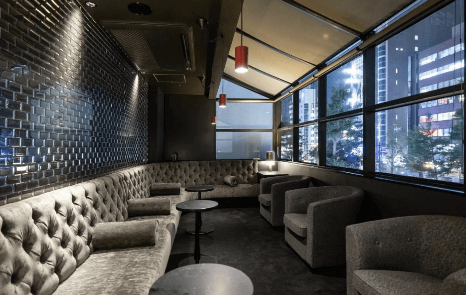 大阪十字飯店 – 歐力士飯店及度假村旗下的精緻休息室或酒吧區。空間裝飾有灰色天鵝絨簇狀扣沙發和扶手椅，以及黑色的圓形茶几。深色的瓷磚牆壁、昏暗的紅色圓筒燈和大片落地窗營造出舒適的氛圍，可觀賞夜晚的城市景觀