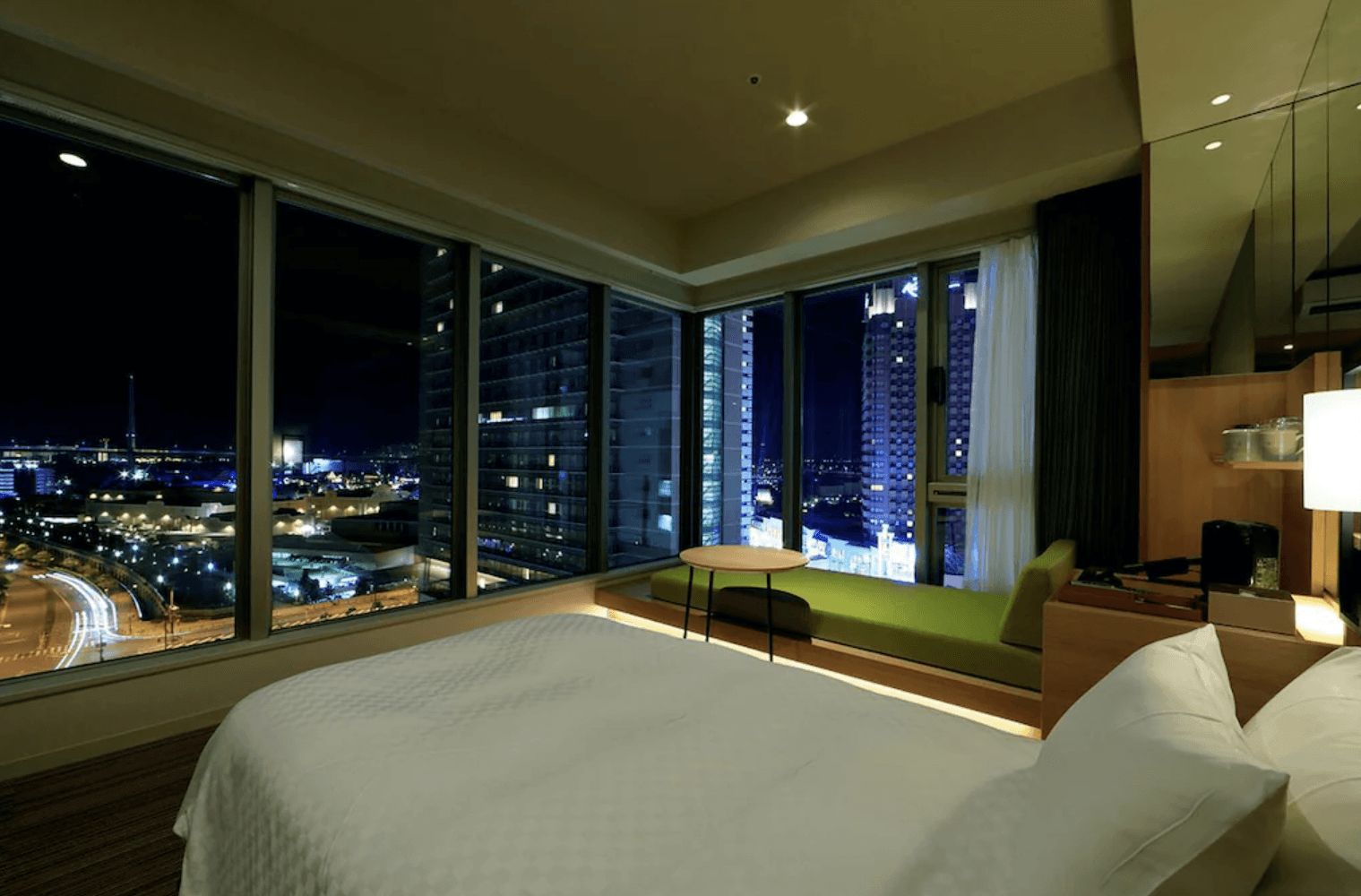 日本環球影城新格拉利飯店及空中水療中心 (The Singulari Hotel & Sky Spa at Universal Studios Japan) 的轉角高樓層客房,房內配備純白床鋪與緊鄰窗邊的綠色休閒長沙發,透過大面積玻璃窗可飽覽絢麗的城市與港灣夜景