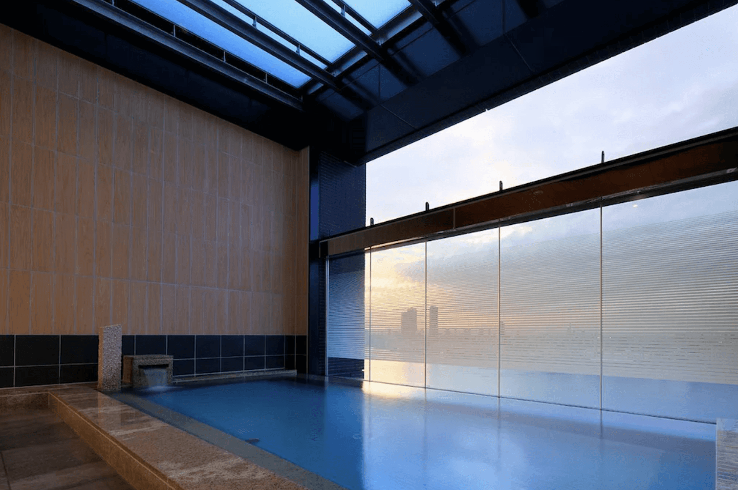 日本環球影城新格拉利飯店及空中水療中心 (The Singulari Hotel & Sky Spa at Universal Studios Japan) 的高空景觀浴池,寬敞的室內水療池結合溫潤的木質牆面,並設有大面玻璃帷幕,讓旅客在放鬆泡湯的同時能眺望遠方朦朧的城市晨昏美景