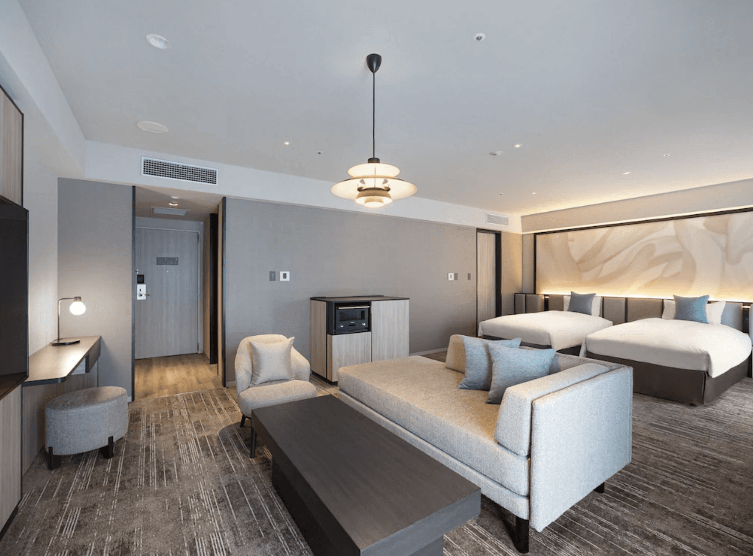 環球城東方飯店 (Oriental Hotel Universal City) 的客房內部視角,畫面呈現出舒適的沙發休息區、迷你吧檯櫃、壁掛電視以及專屬梳妝台,展現現代簡約的住宿環境