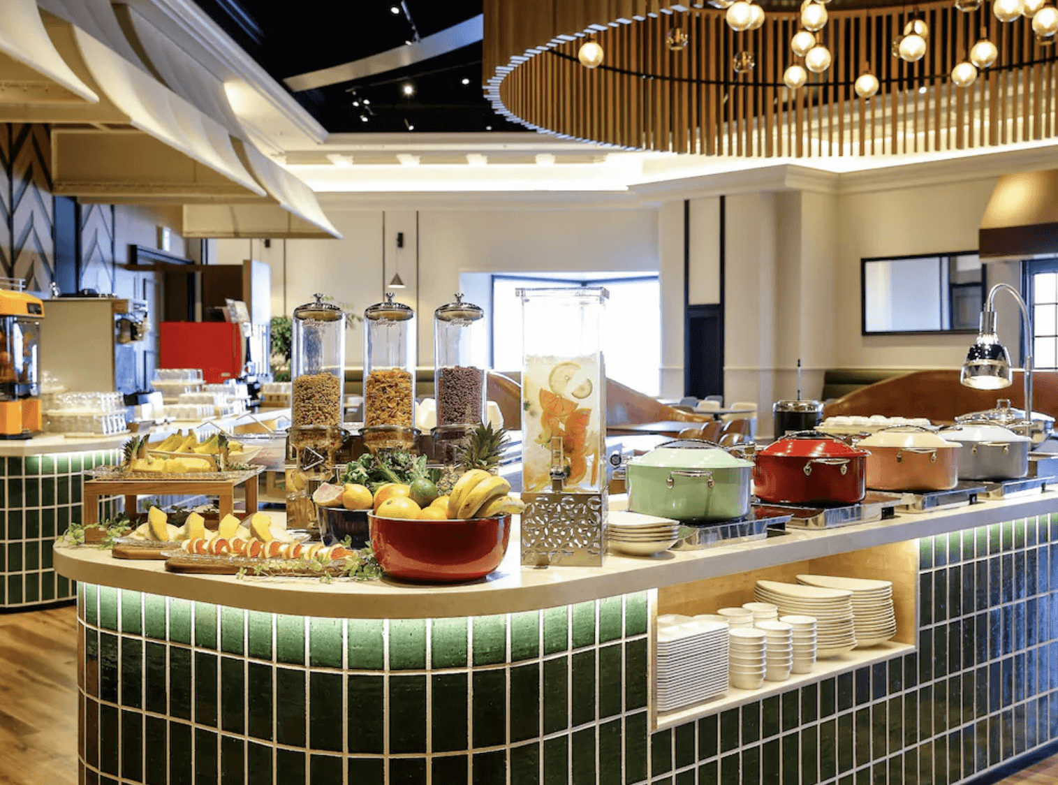 環球城東方飯店 (Oriental Hotel Universal City) 的明亮自助餐廳,復古綠色磁磚的弧形吧檯上陳列著新鮮水果、穀物麥片與色彩繽紛的餐鍋,天花板則裝飾著獨特的圓形木格造型吊燈