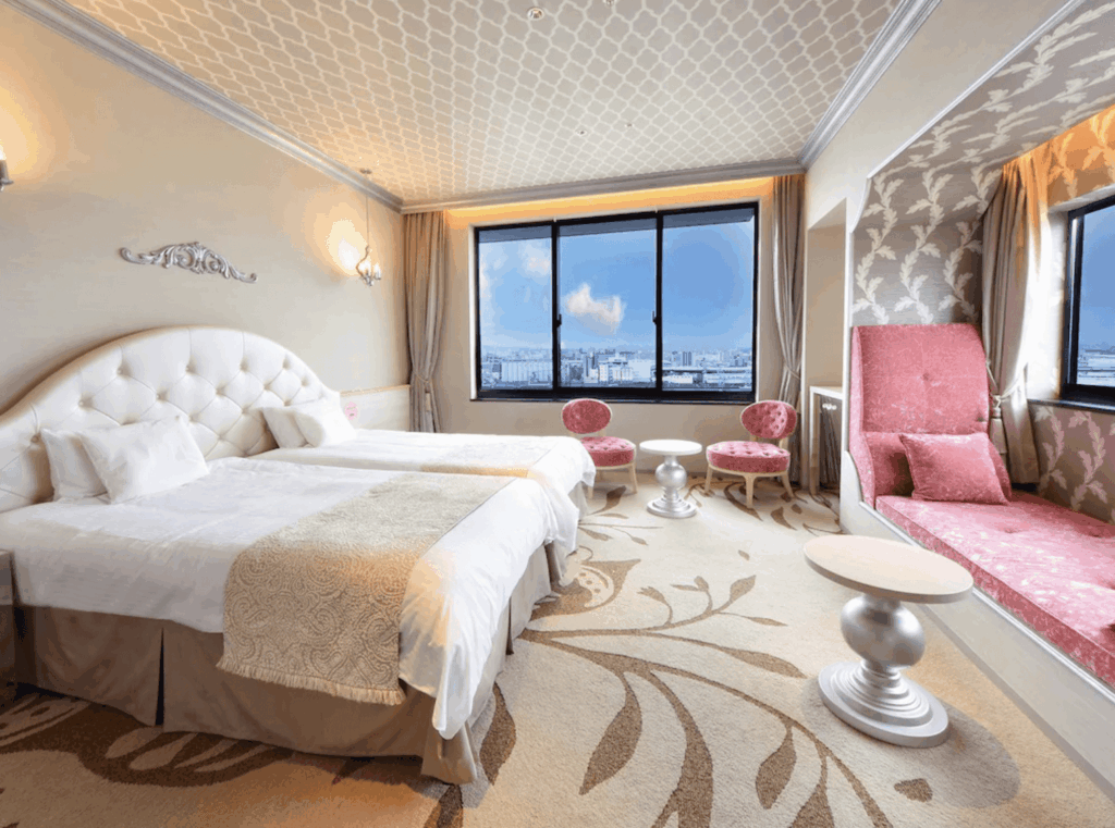 環球影城維塔港酒店 (Hotel Universal Port Vita)的典雅客房，設有白色軟墊床頭板的床位、大面景觀窗戶，以及粉紅色的窗邊沙發休息區與座椅