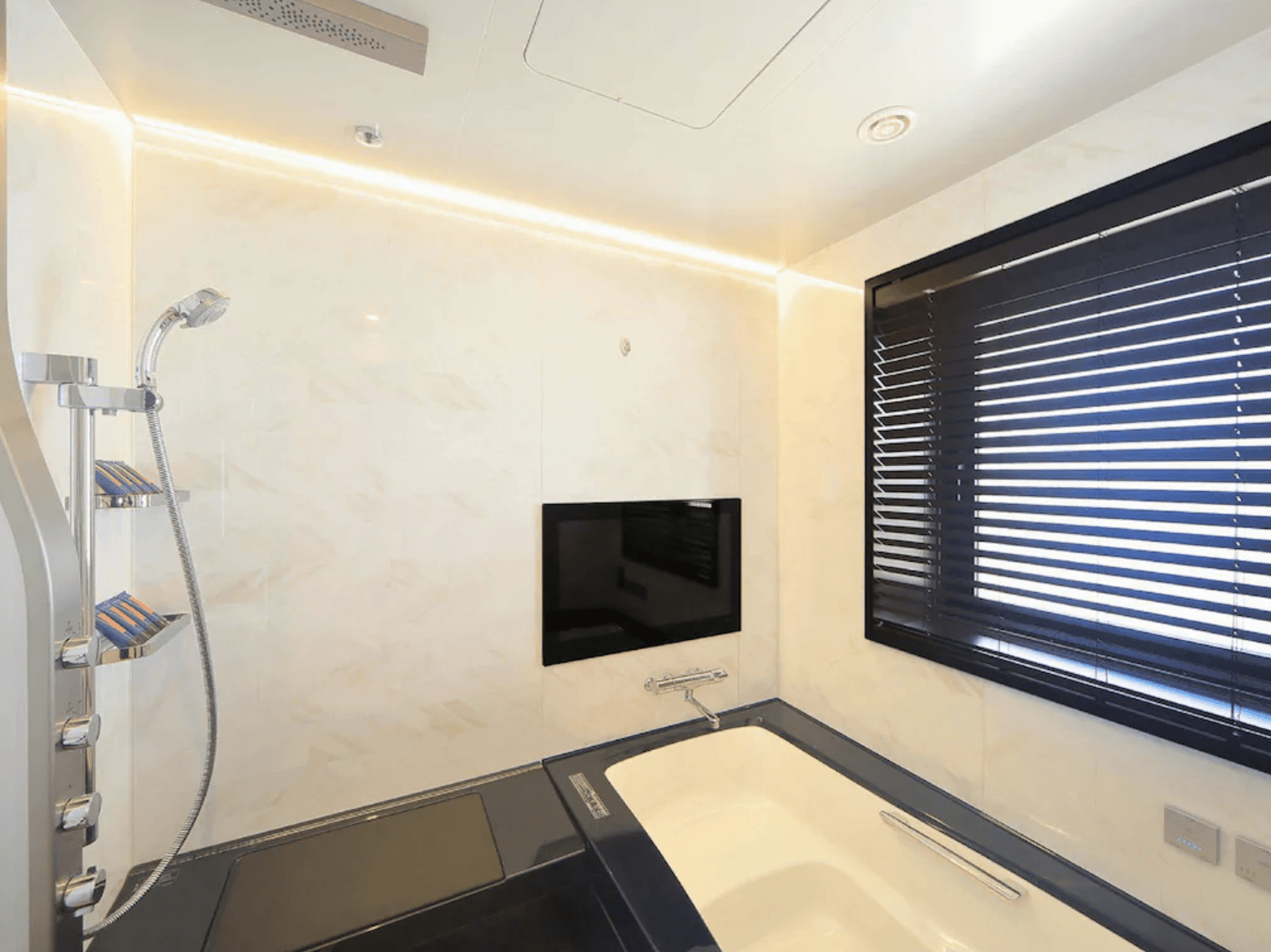 環球影城維塔港酒店 (Hotel Universal Port Vita)的現代化浴室空間,設有黑白對比設計的浴缸,牆面上配有專屬電視螢幕與多功能淋浴設備,並有百葉窗提供採光