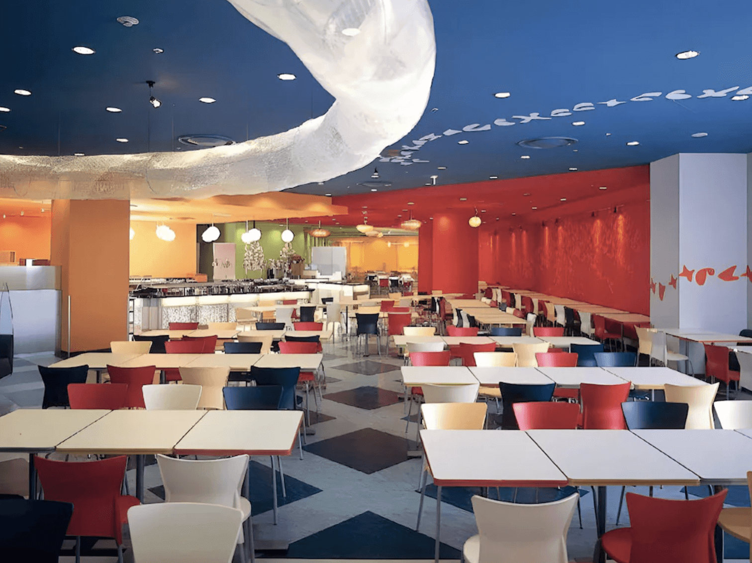 近鐵環球城飯店 (Hotel Kintetsu Universal City) 色彩鮮豔繽紛的自助餐廳。寬敞的空間擁有深藍色的天花板與大型白色波浪狀裝飾,牆面以大面積的橘色、紅色與綠色劃分區域。幾何拼花地板上整齊排列著多組白色餐桌與紅、白、藍等對比色餐椅