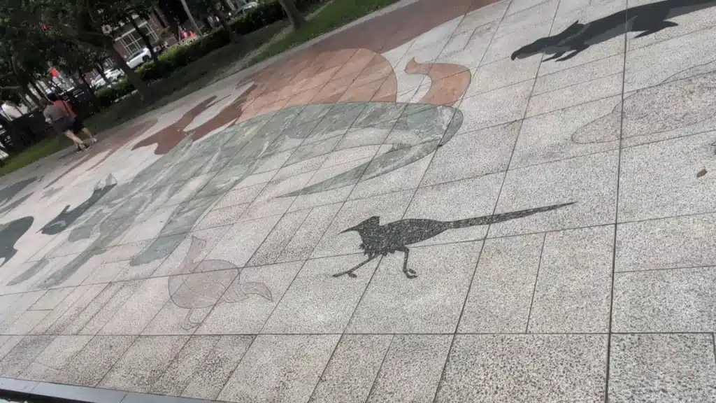 廣場石質鋪面上以不同顏色石材拼貼出的史前生物圖樣，清晰可見巨大恐龍剪影與一隻奔跑的小型恐龍／古鳥類圖形
