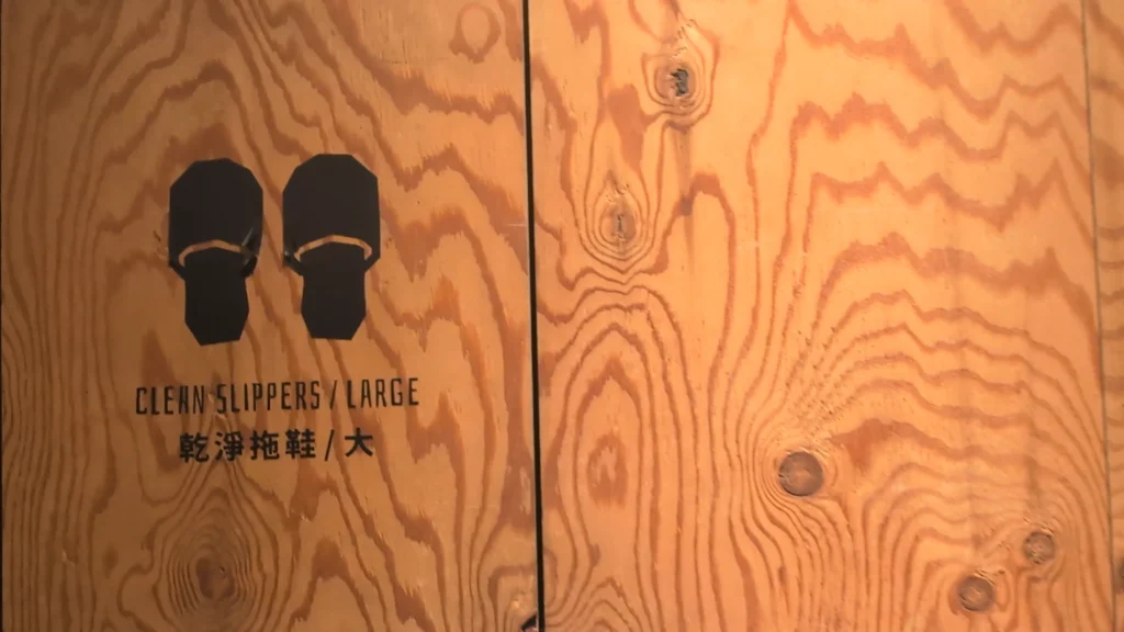 原木紋理鮮明的鞋櫃門板特寫，左側門上清楚標示黑色拖鞋圖示以及「CLEAN SLIPPERS / LARGE 乾淨拖鞋／大」的黑色中英文字樣
